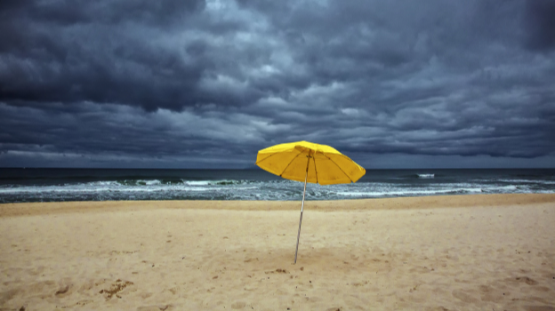 Yellow beach umbrella under stormy clouds.