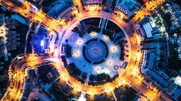 Aerial night view of a large circular roundabout with intersecting roads, illuminated by streetlights and surrounded by buildings