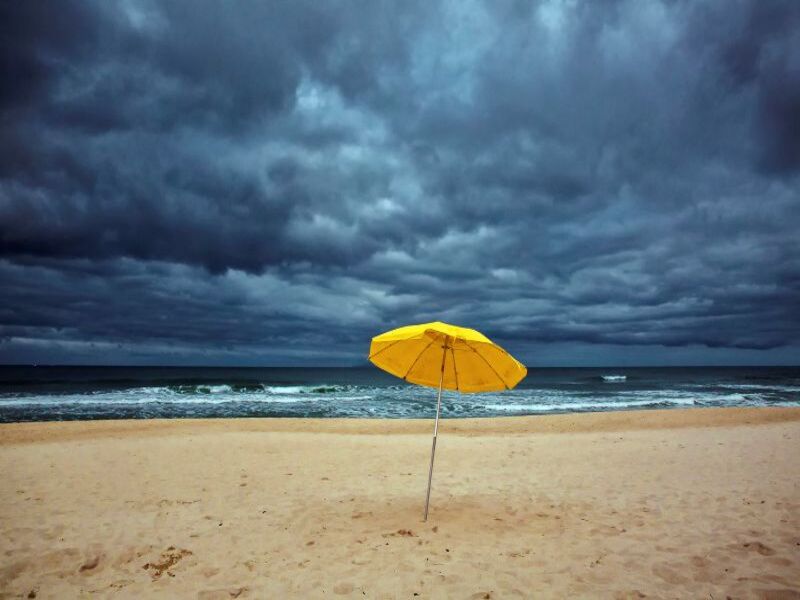 Yellow beach umbrella under stormy clouds.