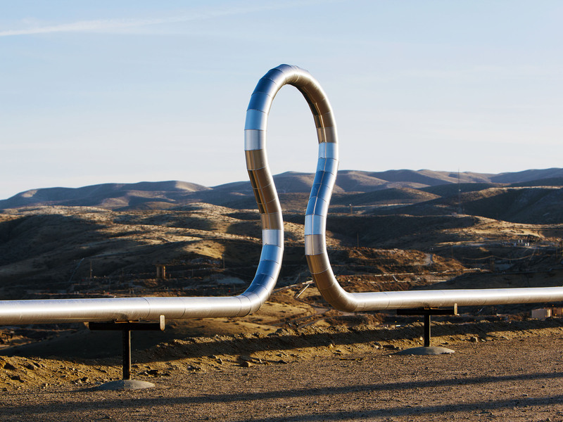 Industrial pipeline forming a loop shape in a dry, mountainous landscape.