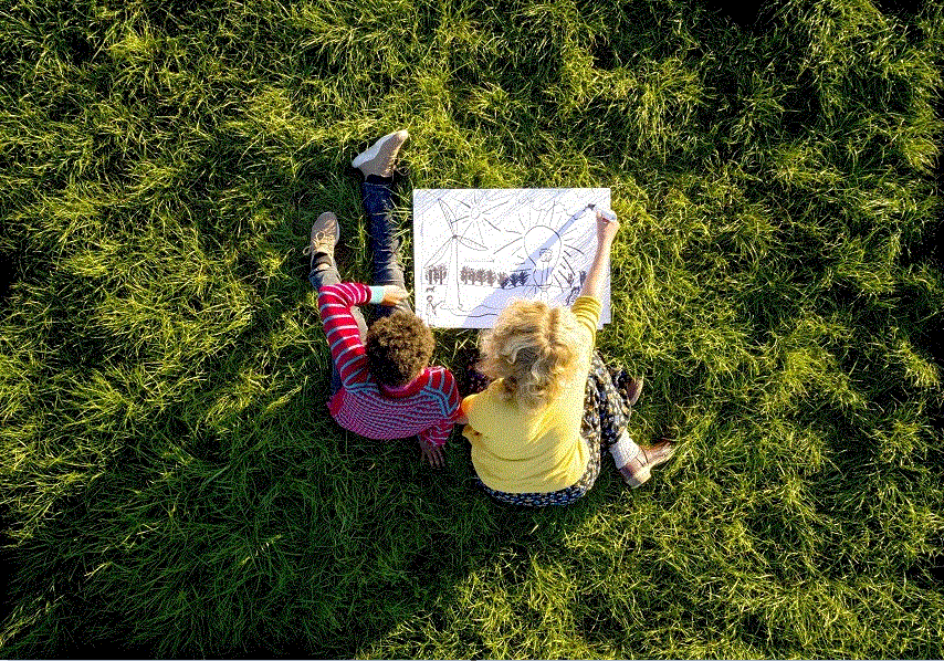 Two young children sitting in grass drawing a picture