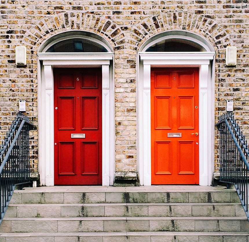 Two attached brick homes, one with a red door and one with an orange door