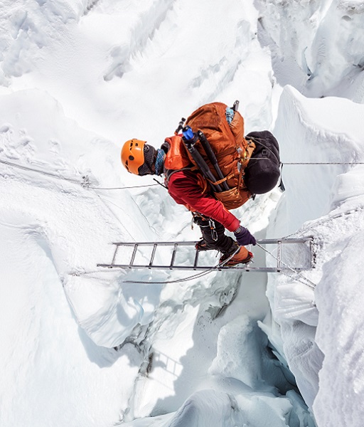 A hiker using a ladder to get across an icy terrain 