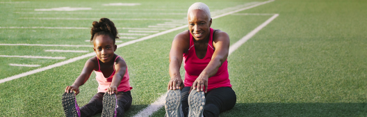Senior woman and young child stretching on field