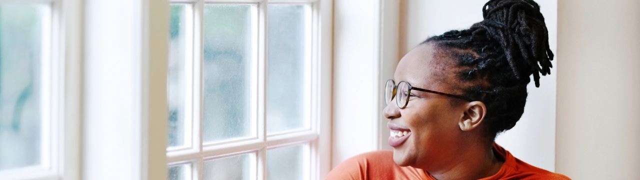 A woman looks out the window, embodying the potential of guaranteed income to revolutionize women's retirement planning.
