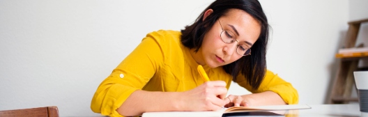 A woman in a yellow shirt writes in a book, symbolizing the importance of planning for emergency savings for retirement.