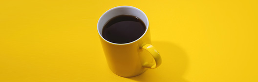 Black coffee in yellow cup with yellow background.