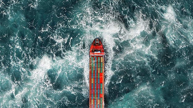An aerial photo shows a cargo ship loaded up with colorful containers on a choppy sea.