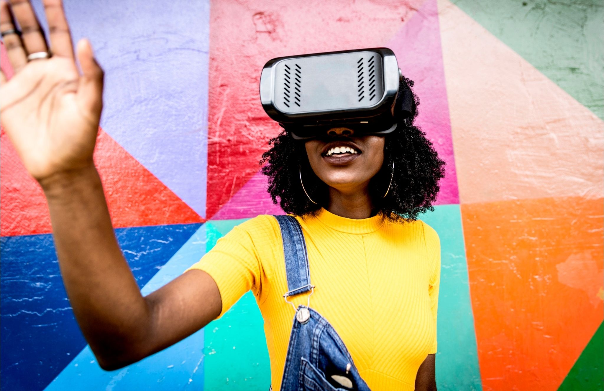 Person wearing a VR headset, raising a hand in front of a colorful mural.