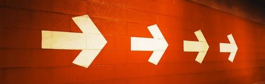 A series of arrows pointing forward on a red brick wall 