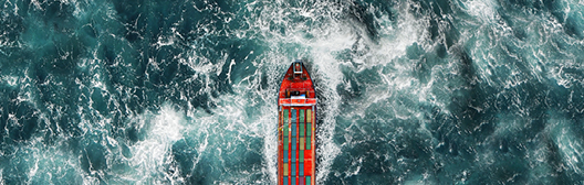 An aerial photo shows a cargo ship loaded up with colorful containers on a choppy sea.
