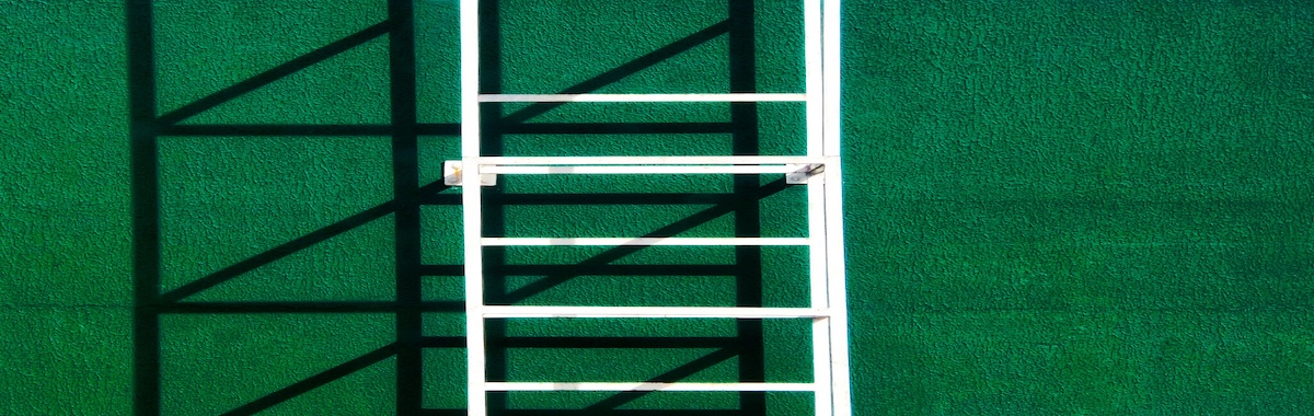 White metal ladder mounted against a textured green wall, casting strong diagonal shadows across the surface.