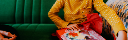Child opening a red gift while sitting on a green couch