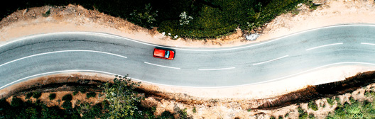 Red car driving in the left lane of a winding road. 