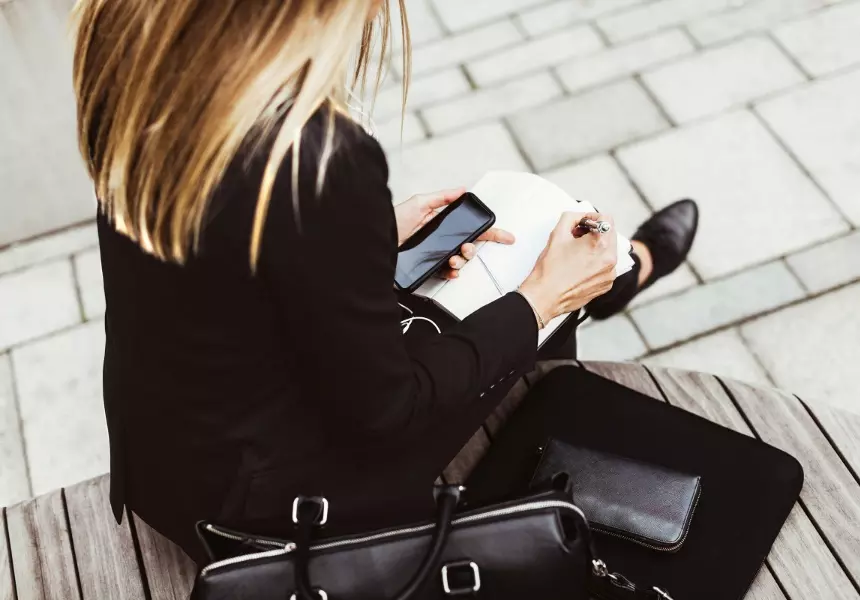 Person seated on a bench using a smartphone and writing notesbeside a briefcase, paired with content promoting retirement resources for financial professional
