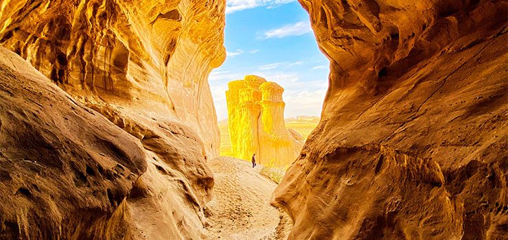 Sunlit sandstone canyon framing a towering rock formation in a desert landscape.