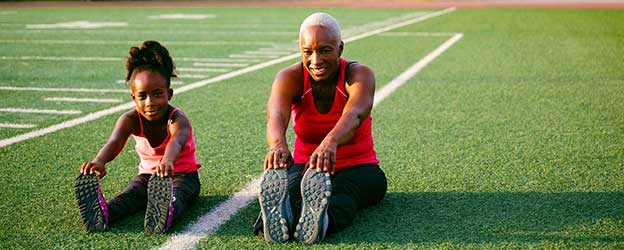 Image of mother and daughter stretching together on a field.
