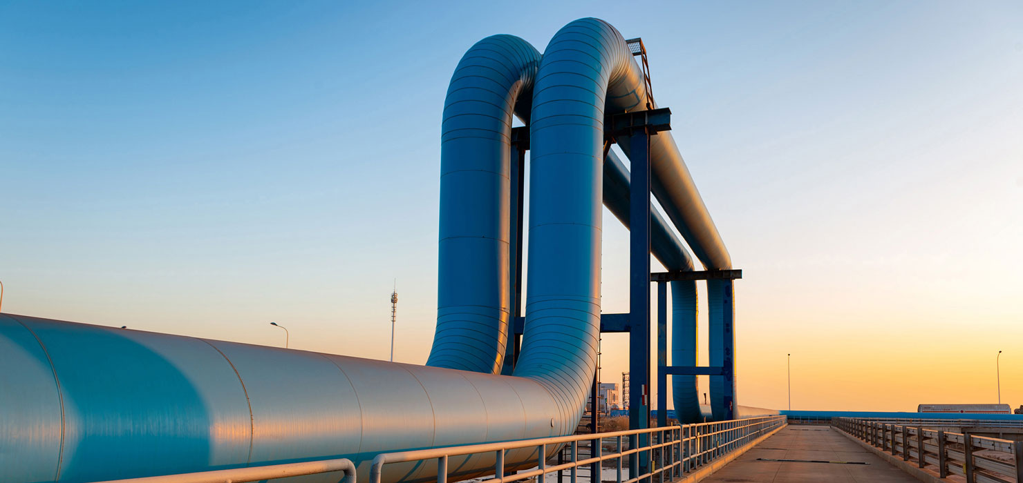 Large blue industrial pipelines curving upward on a concrete platform at sunset.