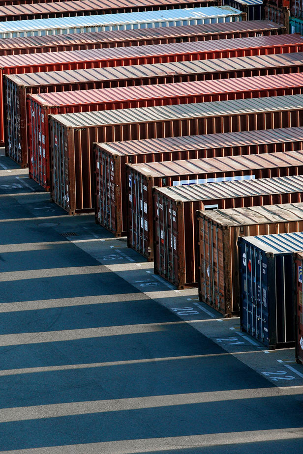Rows of shipping containers casting long striped shadows on pavement.