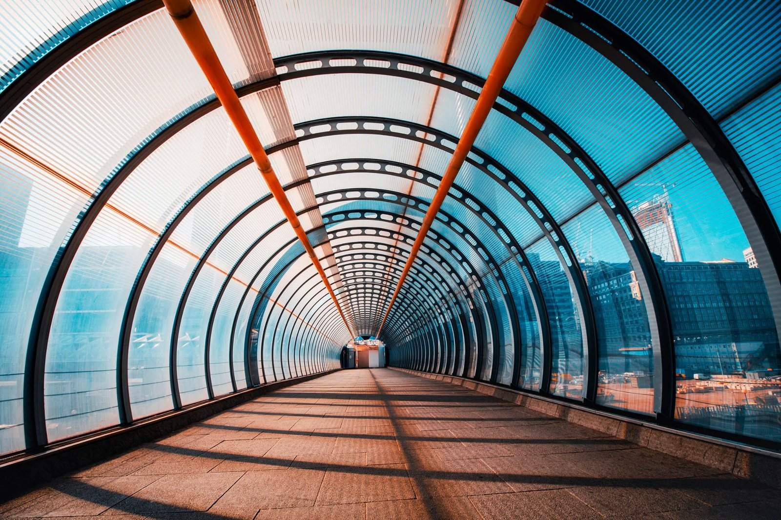 Enclosed pedestrian walkway with curved glass walls and orange structural beams