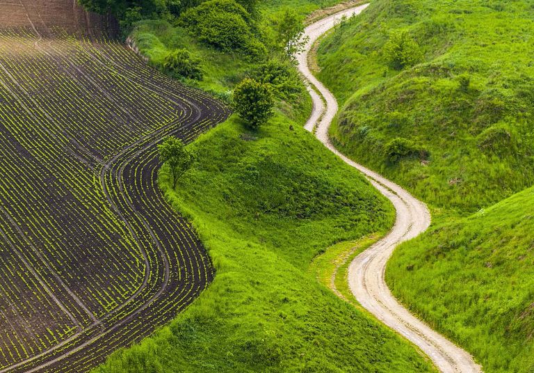 Aerial view of a double lane road cutting through a green valley surrounded by hills and trees.