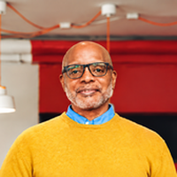 Smiling business owner in a yellow sweater standing inside his restaurant.