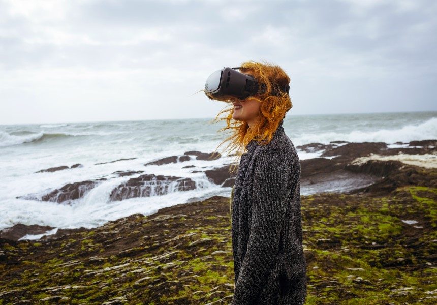 Redhead woman using virtual reality headset in the beach
