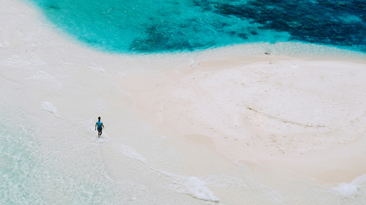 A person strolls on across a white-sand beach.