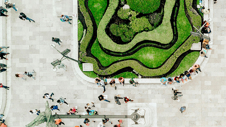 A bird’s eye view of people sitting and walking beside a green park.