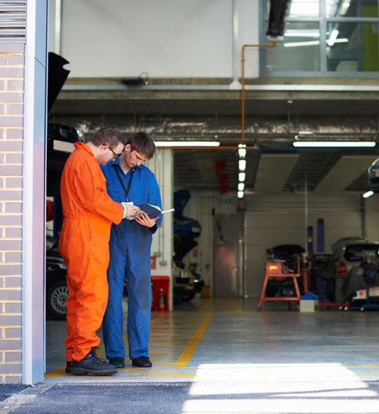 College mechanic students reading manual in repair garage