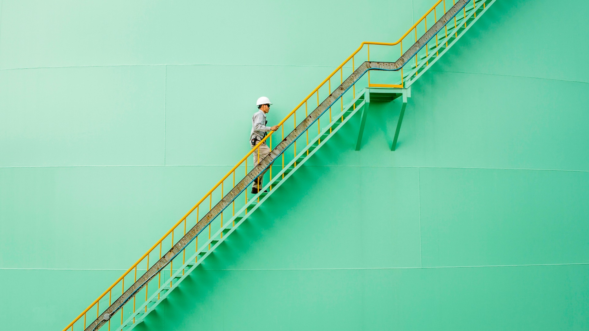 Un homme avec un casque de sécurité monte des escaliers métalliques dans un site industriel