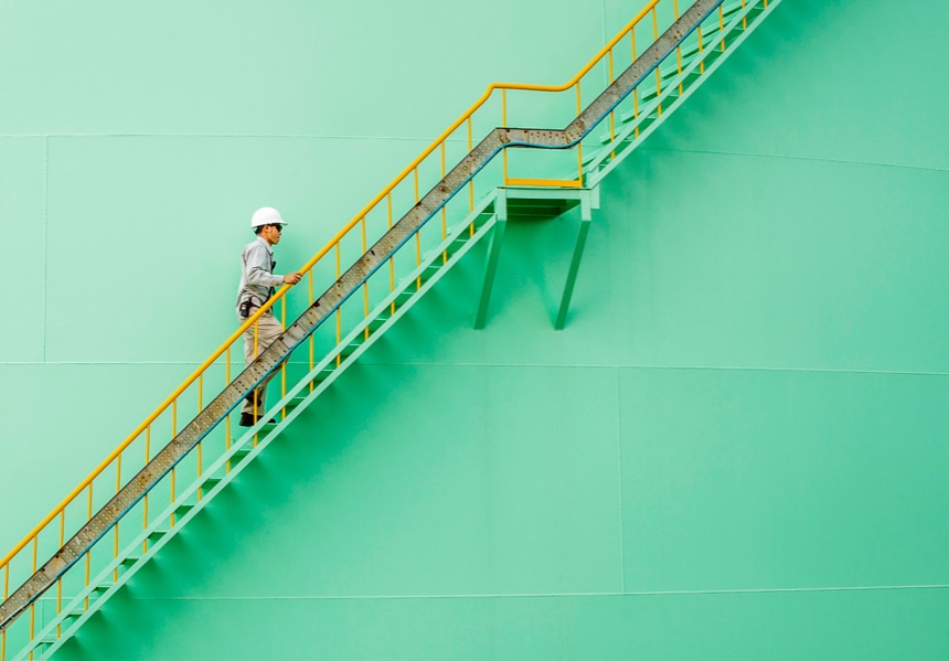 Un hombre con casco subiendo escaleras metálicas en un entorno industrial.