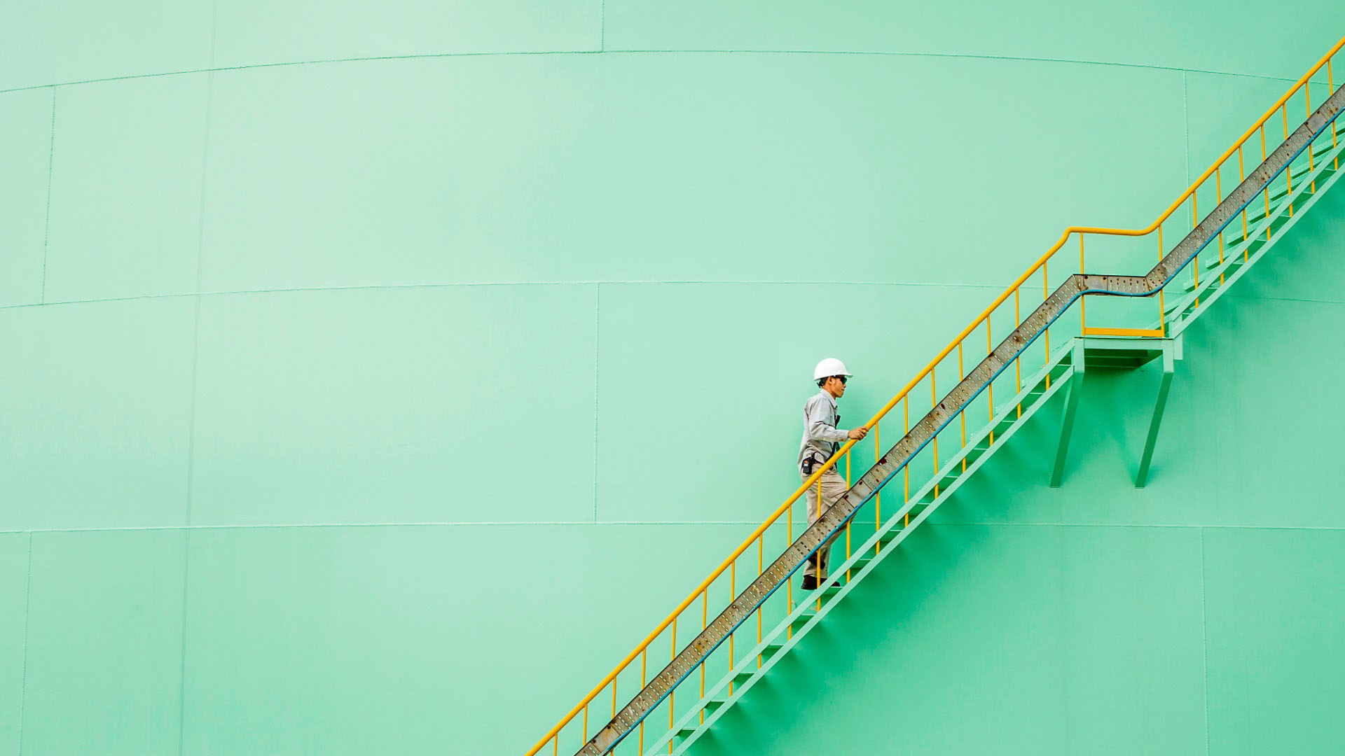 Un hombre con casco subiendo escaleras metálicas en un entorno industrial