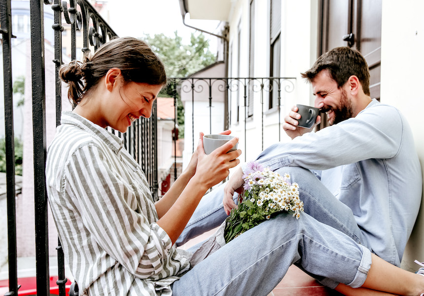 Paar lacht, während es Kaffee trinkt und auf dem Boden eines Balkons sitzt