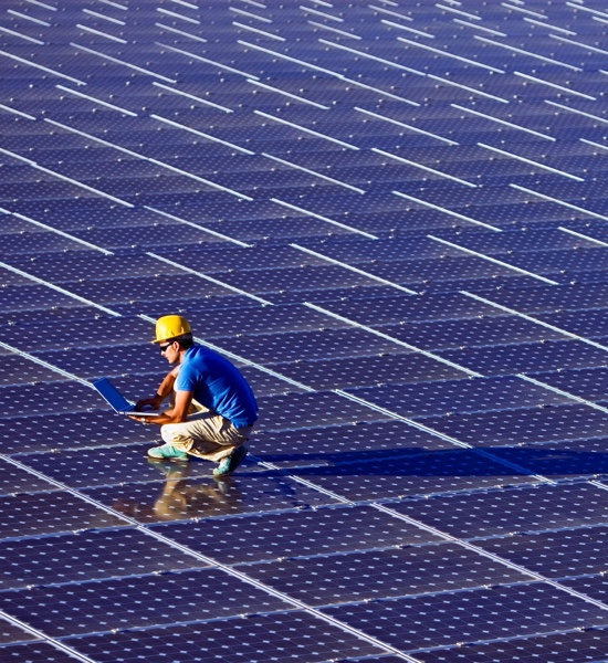 An overhead image of a man squatting over solar panels while on his computer