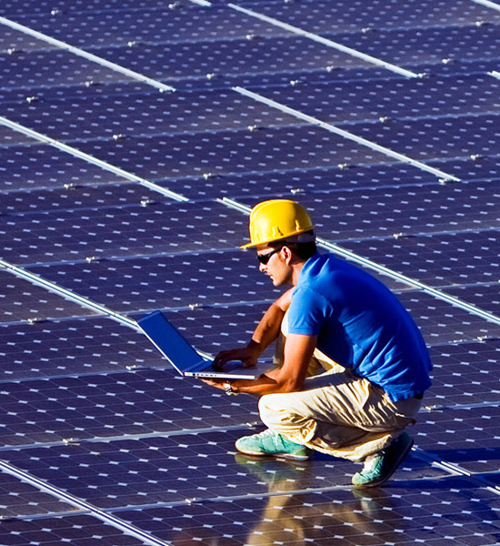 A surface with many solar cells, on which a worker is standing with a laptop.