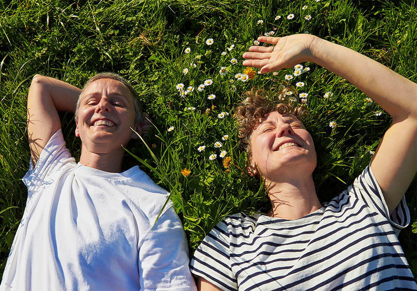 Zwei Frauen liegen lachend auf einer Blumenwiese.