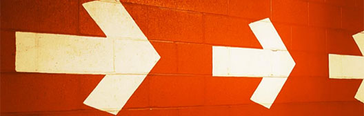 Drei Pfeile zeigen nach rechts auf einer orangefarbenen Betonwand.