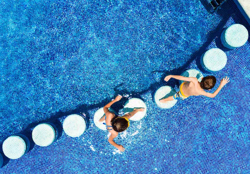 Bambini che giocano sul bordo di una piscina sotto il sole splendente.