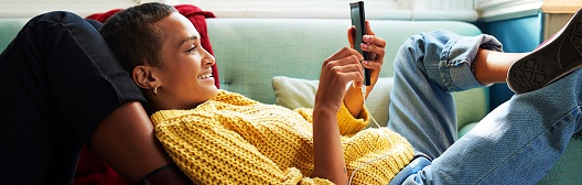 Een vrouw ligt comfortabel op de bank en kijkt op haar mobiele telefoon.