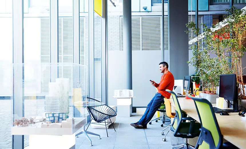 A photo of a man leaning on his desk in an office building.