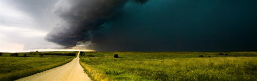 Un paesaggio drammatico con una nuvola tempestosa che si forma sopra una strada tra campi verdi, a simboleggiare la volatilità e l’incertezza del mercato.