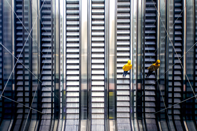 A person standing on an escalator, wearing casual yellow clothing
