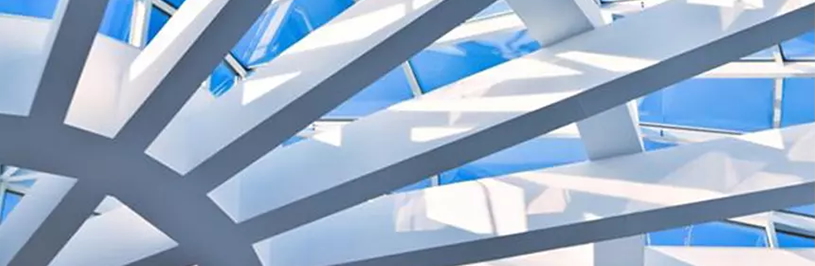 Modern architectural ceiling with intersecting white beams and large glass panels with a bright blue sky above.