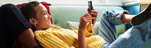 Een vrouw ligt comfortabel op een bank en kijkt op haar mobiele telefoon.