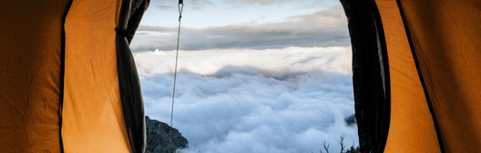 Uitzicht vanuit een tent op bergen boven de wolken bij zonsopkomst.