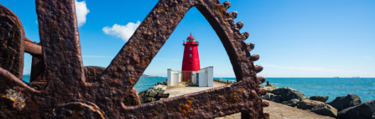 : A red lighthouse seen through a rusty metal frame