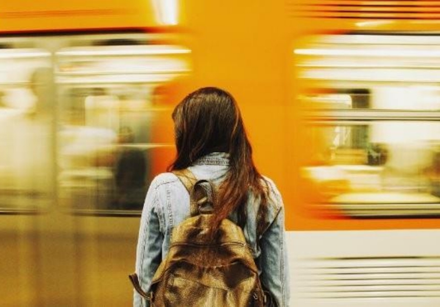 Une personne immobile, vue de dos sur un quai, fait face au passage rapide et flou d’un métro, symbolisant l’attente au cœur du mouvement urbain.