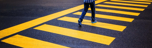 Person walking across a yellow striped pedestrian crosswalk on a paved road