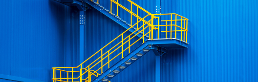 Zigzag yellow metal staircase with safety railings on the exterior of a blue industrial building